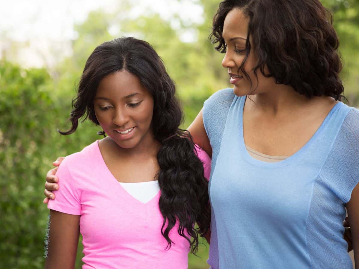 Young teen in pink shirt with her mother wearing blue; the mother's arm is around her daughter