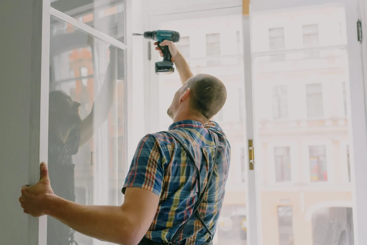 Man in plaid shirt installing window frame with drill