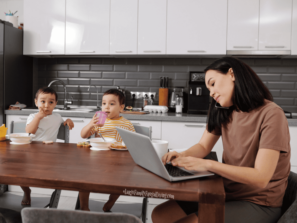 Mother on laptop at kitchen table with young children 