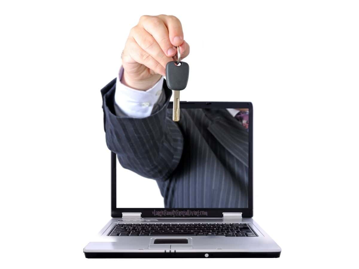 A laptop sitting open in white space with a hand holding a car key coming out of the screen