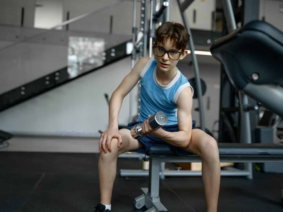 Skinny boy wearing big glasses lifting a dumbbell.