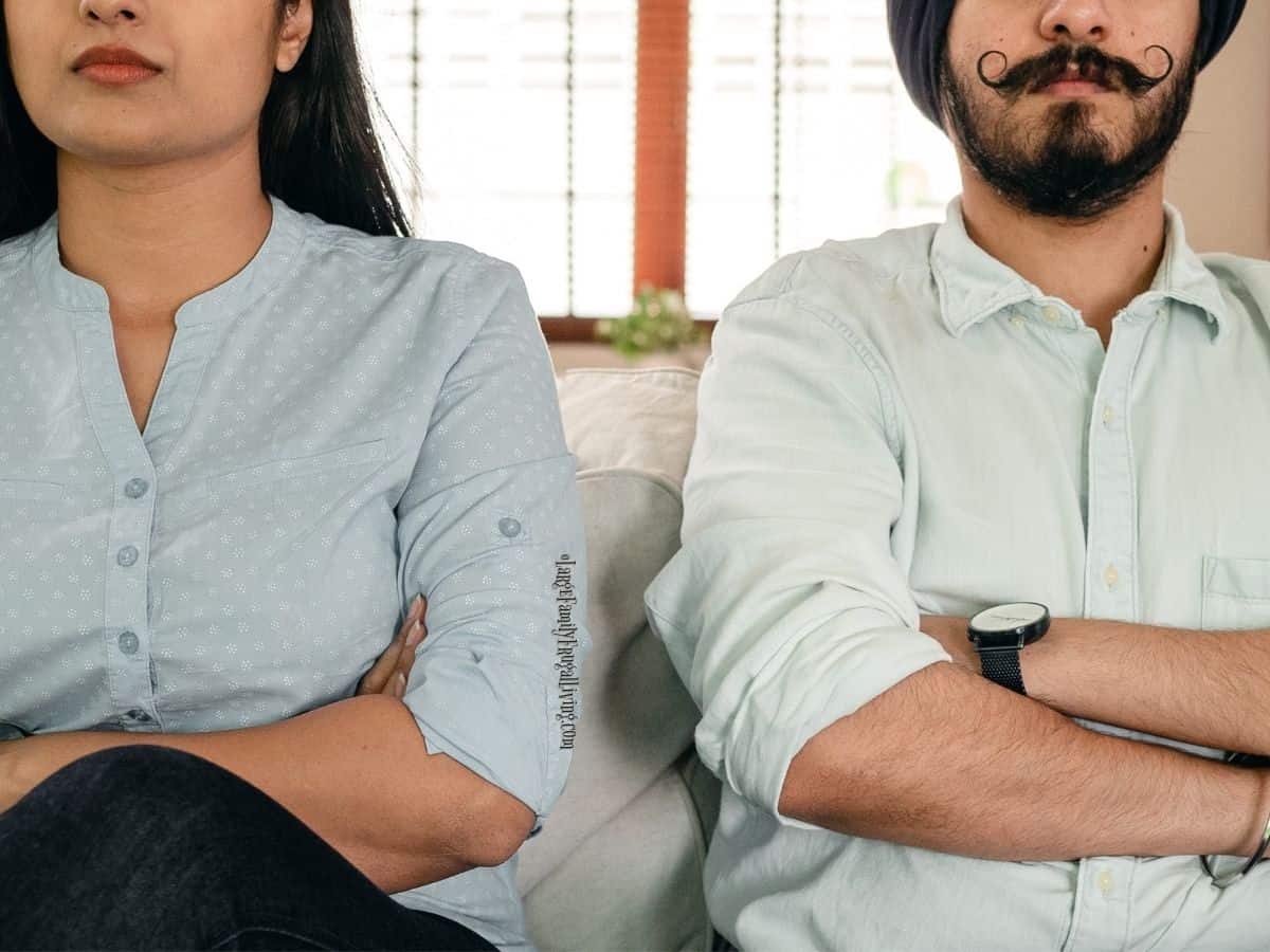 Serious couple with crossed arms sitting beside each other on couch.