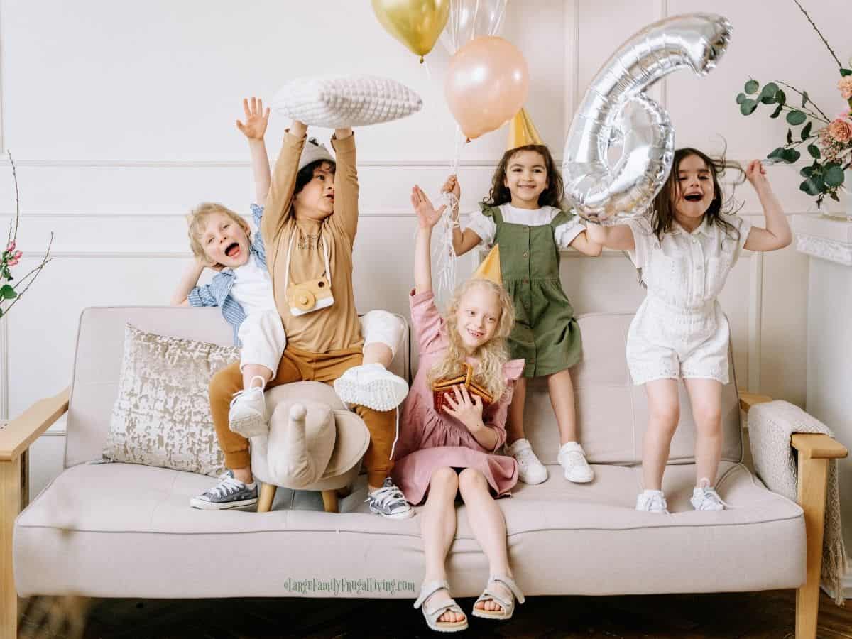 Happy children sitting and standing on sofa celebrating a birthday with balloons