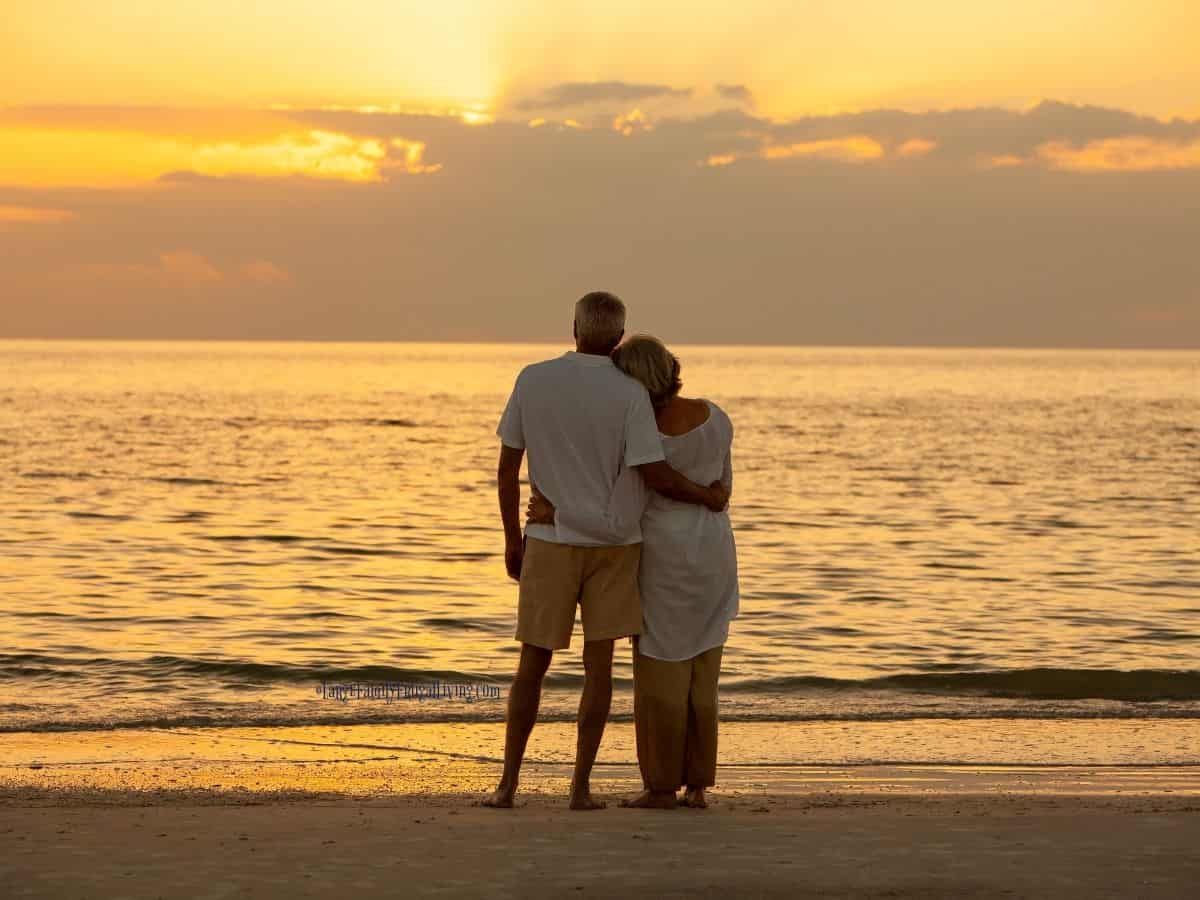 Couple standing beside each other, arms around each other watching sunset on beach