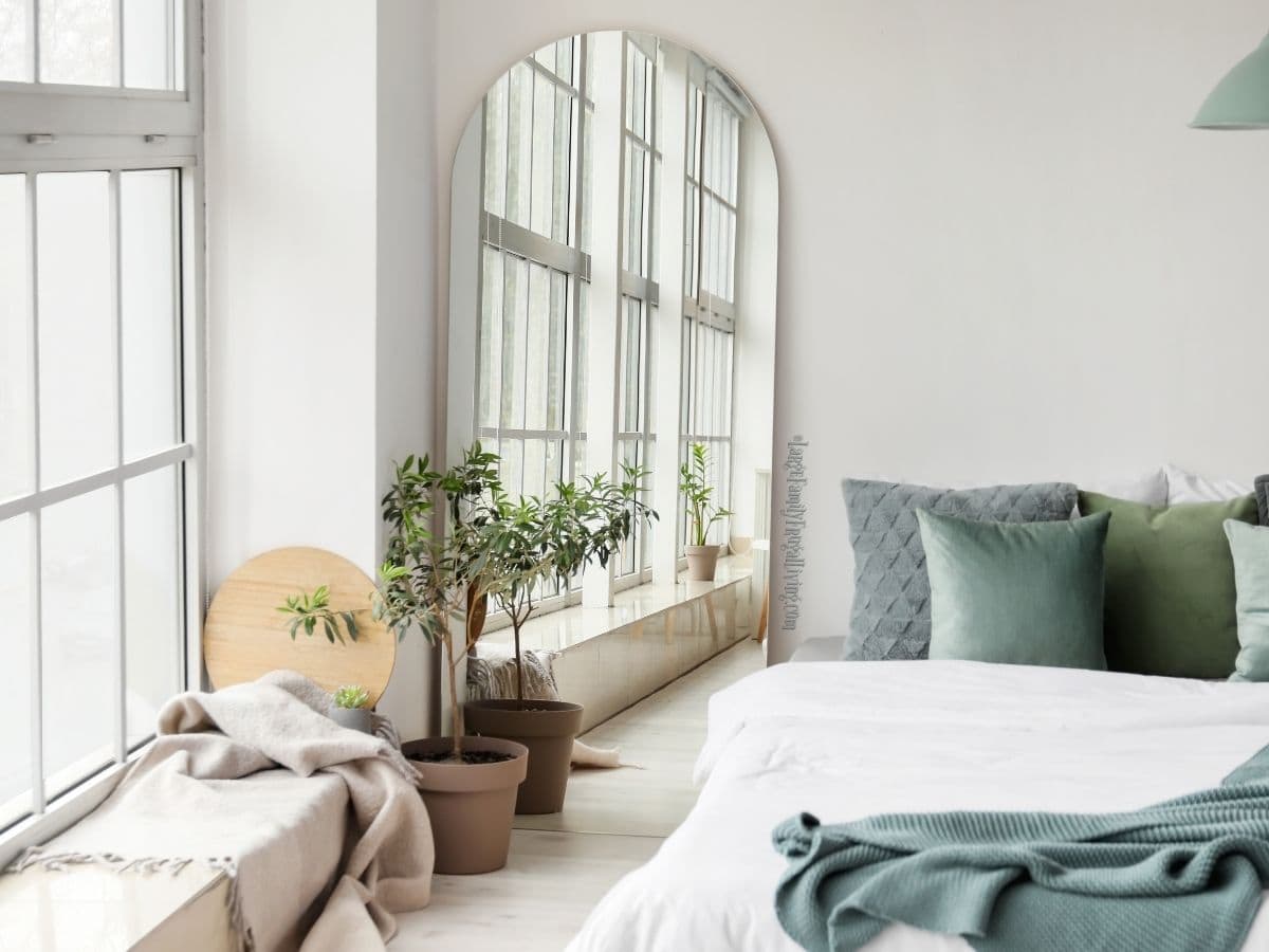 Bright white bedroom with large window array and arched mirror - soft green decor and potted plant