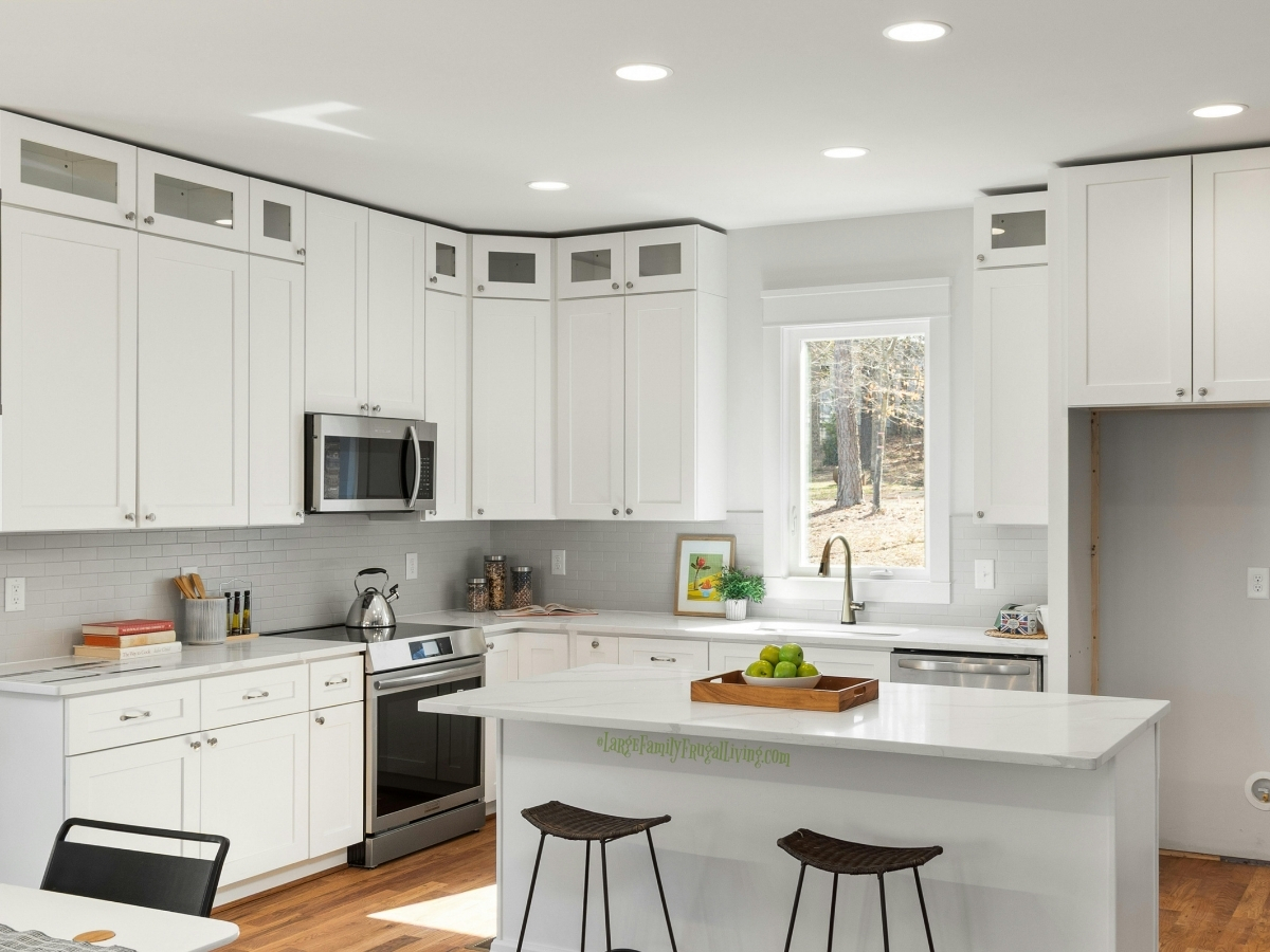 Clean white kitchen with island on medium brown wood floor and woven brown bar stools