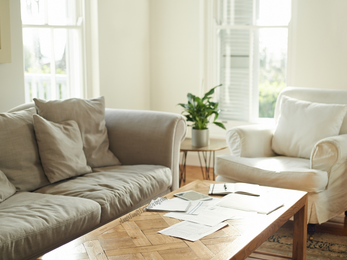 Soft upholstered sofa and chair around wood coffee table with bright windows behind