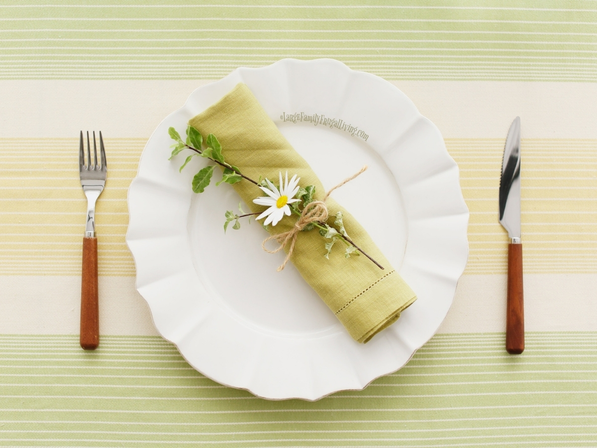 Daisy tied on green cloth napkin laying on white dinner plates set on a green and yellow striped tablecloth