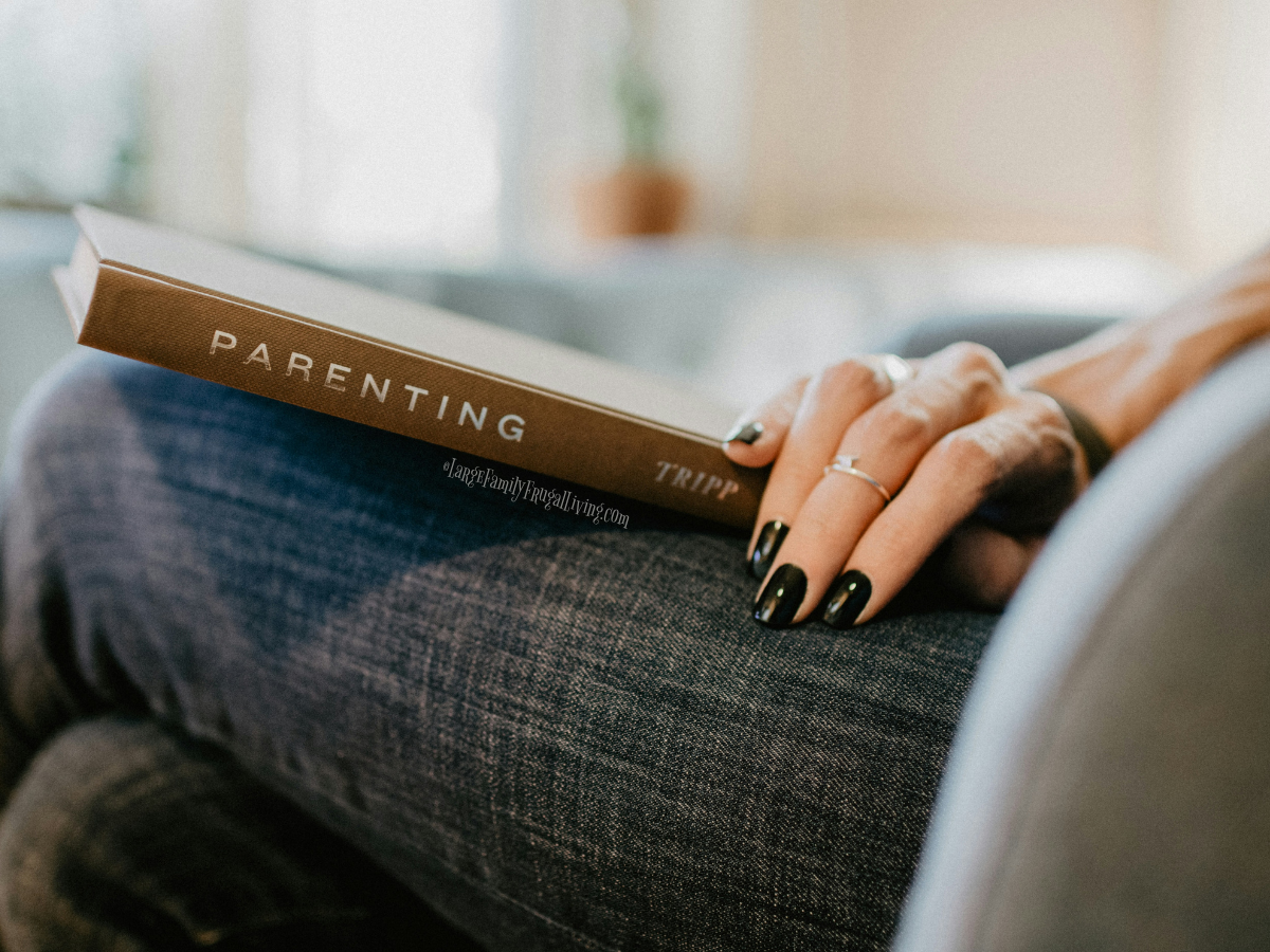 Brown hard cover book titled Parenting on a woman's lap; her legs are crossed and her hand is resting on top.