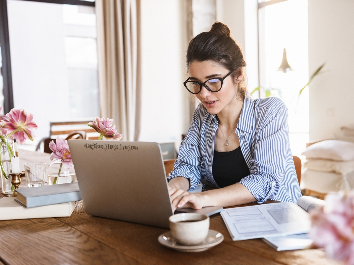 Woman wearing glasses working on laptop at a table with flowers and cup of tea
