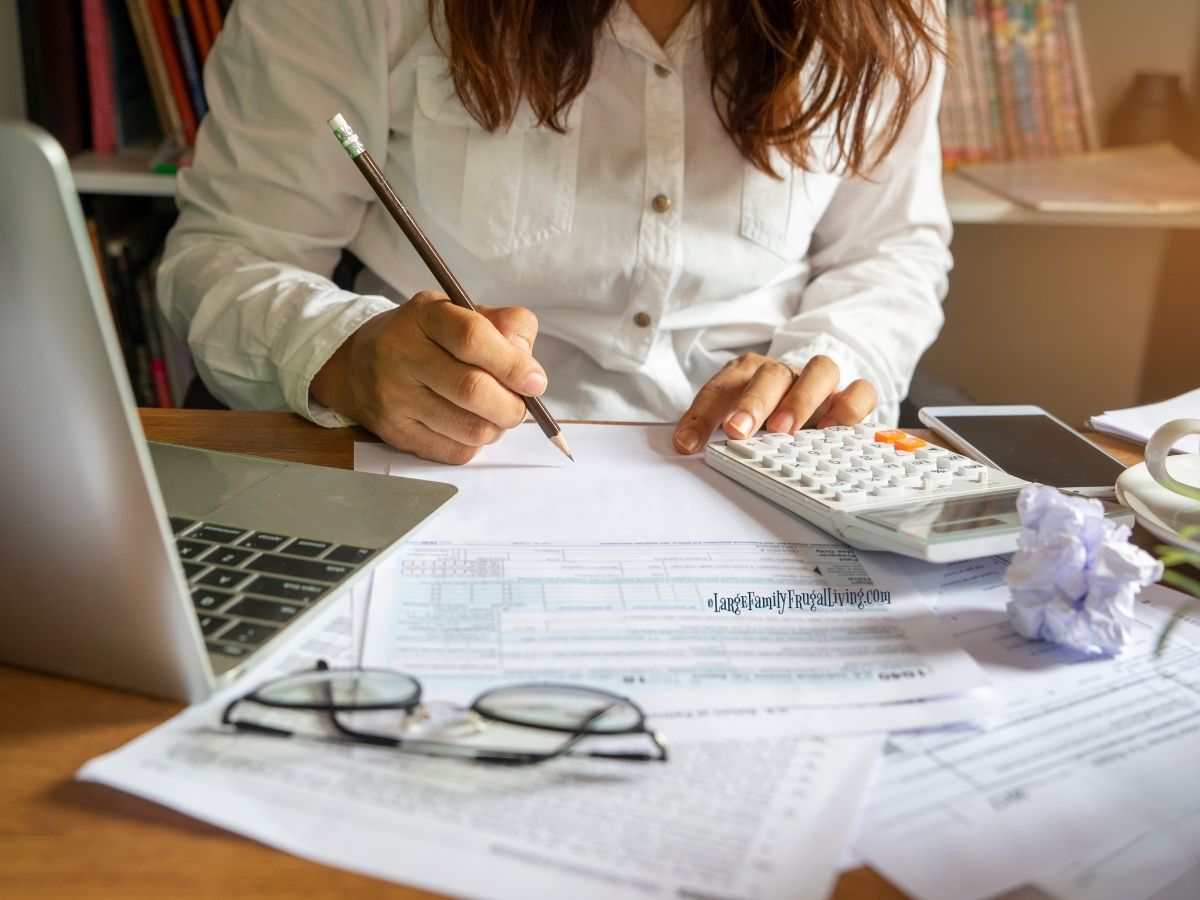 Woman at table with laptop, calculator, and forms; a pencil is in her hand