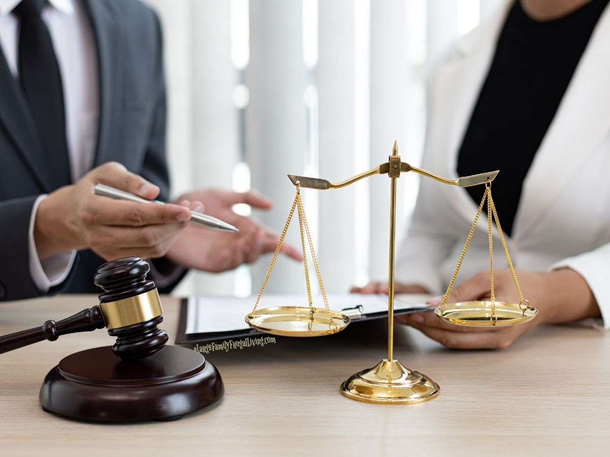 Two people at a desk, seen from shoulders down, justice scales and gavel on desk; they are discussing papers between them